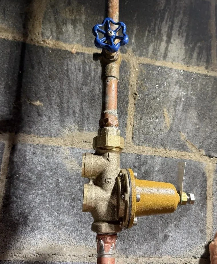 Copper water line with a brass valve assembly and blue shutoff handle