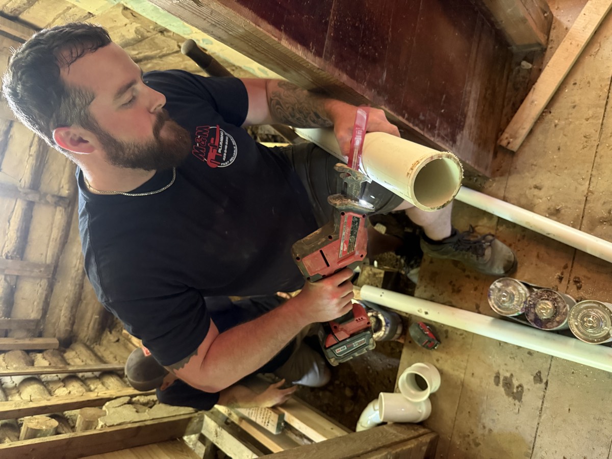 M & M Plumbing technician cutting and replacing PVC pipe on a repair job